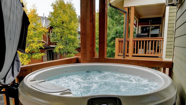 Ein Whirlpool auf einer Holzterrasse, mit Bedienfeld, umgeben von Bäumen und einem Haus im Hintergrund.