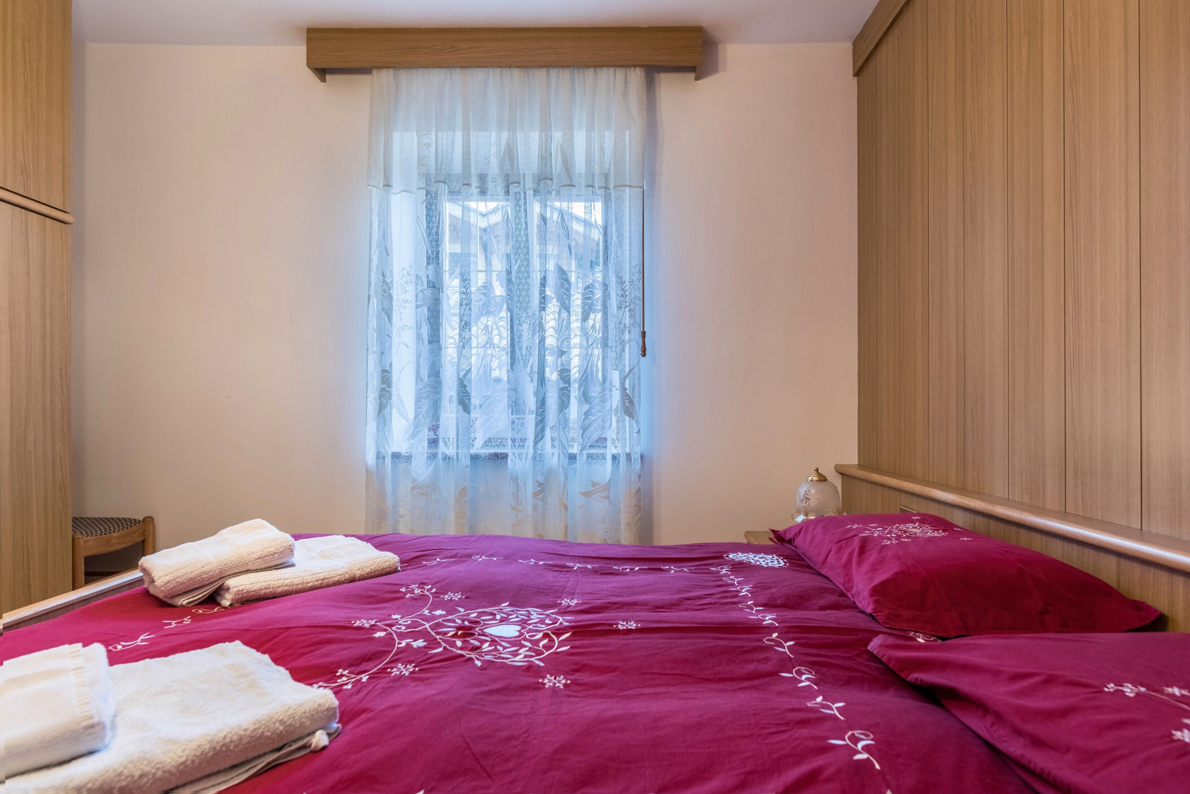 Une chambre à coucher avec un lit, des oreillers, une fenêtre avec des rideaux légers et une tête de lit en bois.