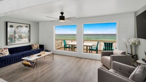 Una sala moderna con vista al océano, un ventilador de techo y un amplio ventanal que da a una terraza.