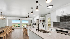 Una cocina moderna con armarios blancos, una isla grande con pileta e iluminación colgante.