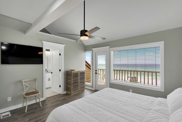 A bedroom with a large bed, a ceiling fan, a TV, and a view of the ocean through a balcony. - Luxurious Gulf Front Home with Private Beach – Newly Renovated in Destin! (Destin)