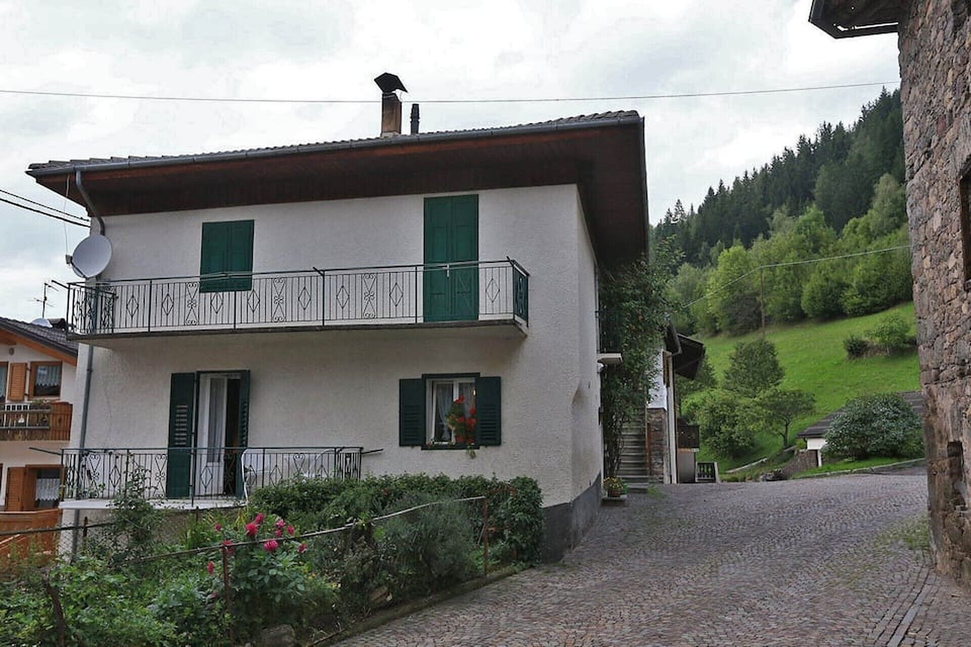 A two-story building with a balcony, a satellite dish, and a stone wall.
