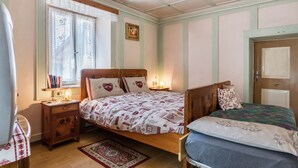 Un dormitorio con dos camas, una mesita de noche, una ventana con cortinas, un cuadro enmarcado y una puerta.