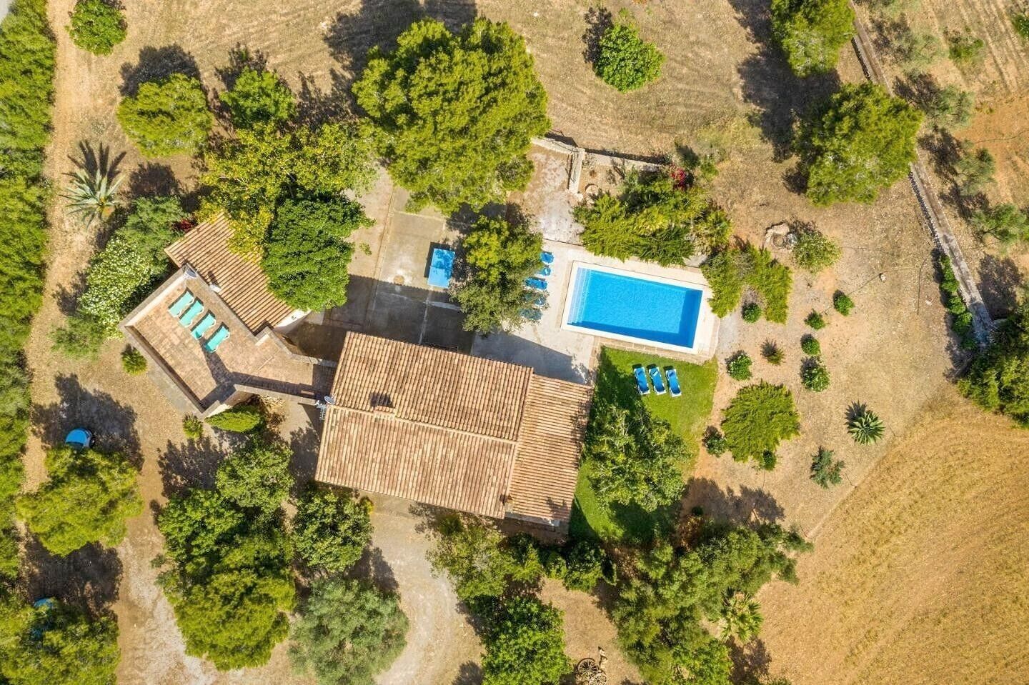 An aerial view of a property with a swimming pool, a patio with lounge chairs, and a large building with a tiled roof.