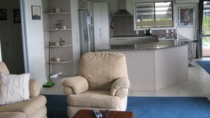 A modern kitchen with a built-in island, a beige armchair, and a dining area with a blue carpet.