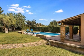 Una piscina con sillas de descanso, un patio de piedra y una zona de estar cubierta.