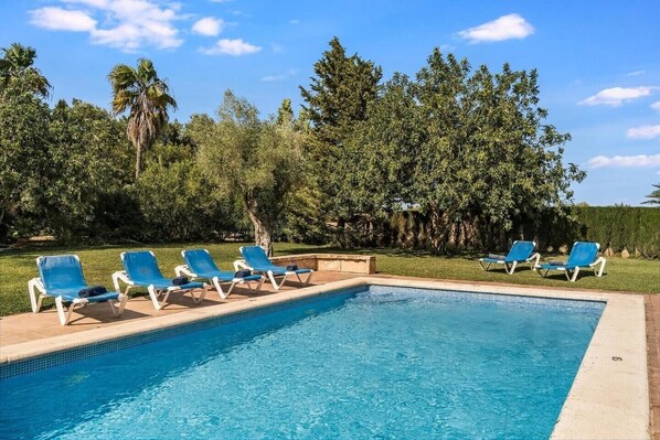 Una piscina con sillas azules y un área verde con árboles.