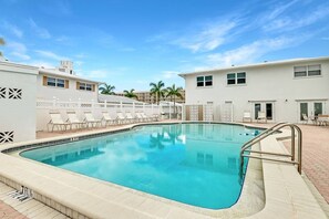 A swimming pool with lounge chairs and a white building with patterned walls. - Private Beach Villa: Modern Luxury at Crystal Sand (Siesta Key)