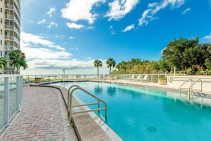 A swimming pool with a curved edge, surrounded by a glass railing, and adjacent to a building with multiple balconies. - Private Beach Villa: Modern Luxury at Crystal Sand (Siesta Key)