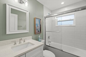 A bathroom with a white sink, two faucets, a toilet, and a glass-enclosed shower with a window. - Private Beach & Gulf-Front Pool Modern Free-Standing Villa at Crystal Sands (Siesta Key)