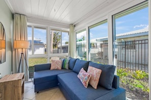 A room with a sectional sofa, a lamp, and large windows offering a view of the outside.