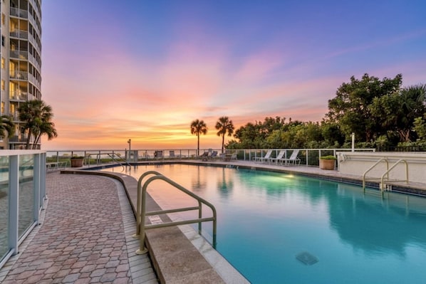 A swimming pool with a sunset view, surrounded by palm trees and a building. - Private Beach & Gulf-Front Pool Modern Free-Standing Villa at Crystal Sands (Siesta Key)