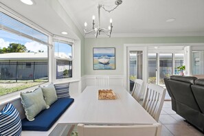 A dining area with a white table, blue cushioned bench, and a painting of a boat. - Private Beach & Gulf-Front Pool Modern Free-Standing Villa at Crystal Sands (Siesta Key)