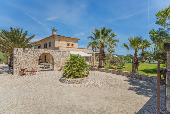 A stone building with a tiled roof, surrounded by palm trees and a paved courtyard.
