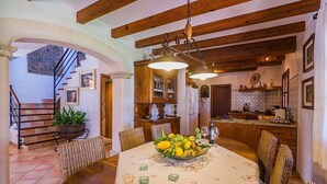 Un comedor con una mesa de madera, sillas, una araña y una escalera que lleva a otra habitación.