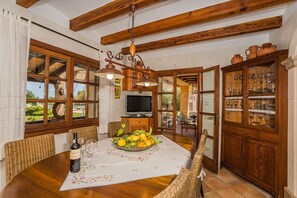 A dining area with a wooden table, wicker chairs, a TV, and a view of the outdoors.