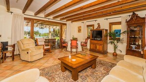 Un salón espacioso con techo de madera, televisor, comedor con sillas y un ventanal grande.