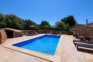 Une piscine rectangulaire entourée de murs de pierre et de verdure, avec des chaises longues et des parasols.