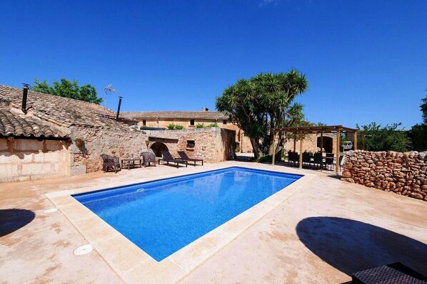 Una piscina con lettini, una pergola e pareti in pietra.