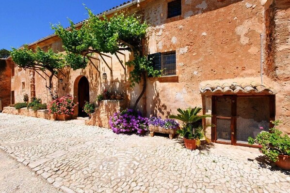 Un bâtiment rustique doté d’une cour pavée, d’arcades et de plantes en pot.