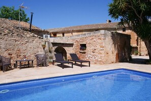 Una piscina con lettini e un tavolo, un muro in pietra e un cielo azzurro limpido.