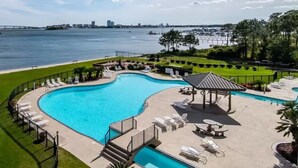 A swimming pool with lounge chairs and a gazebo, surrounded by a well-maintained lawn and a view of a body of water with a bridge in the distance. - Back Bay 1106 | Panoramic Views | Spacious Waterfront Penthouse | My Beach Getaways (Orange Beach)