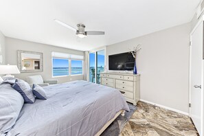 Une chambre à coucher avec un lit, un téléviseur, une commode, un ventilateur de plafond et une vue sur la ville.