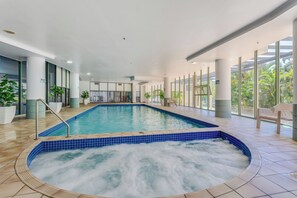 Piscina interior con hidromasaje, rodeada de grandes ventanales y plantas en macetas.