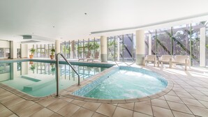 An indoor swimming pool with clear water, surrounded by tiled flooring, and equipped with a metal ladder.