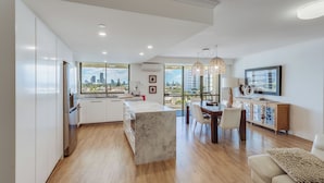 A modern kitchen with a central island, dining area with chairs, a sofa, and a TV mounted on the wall.