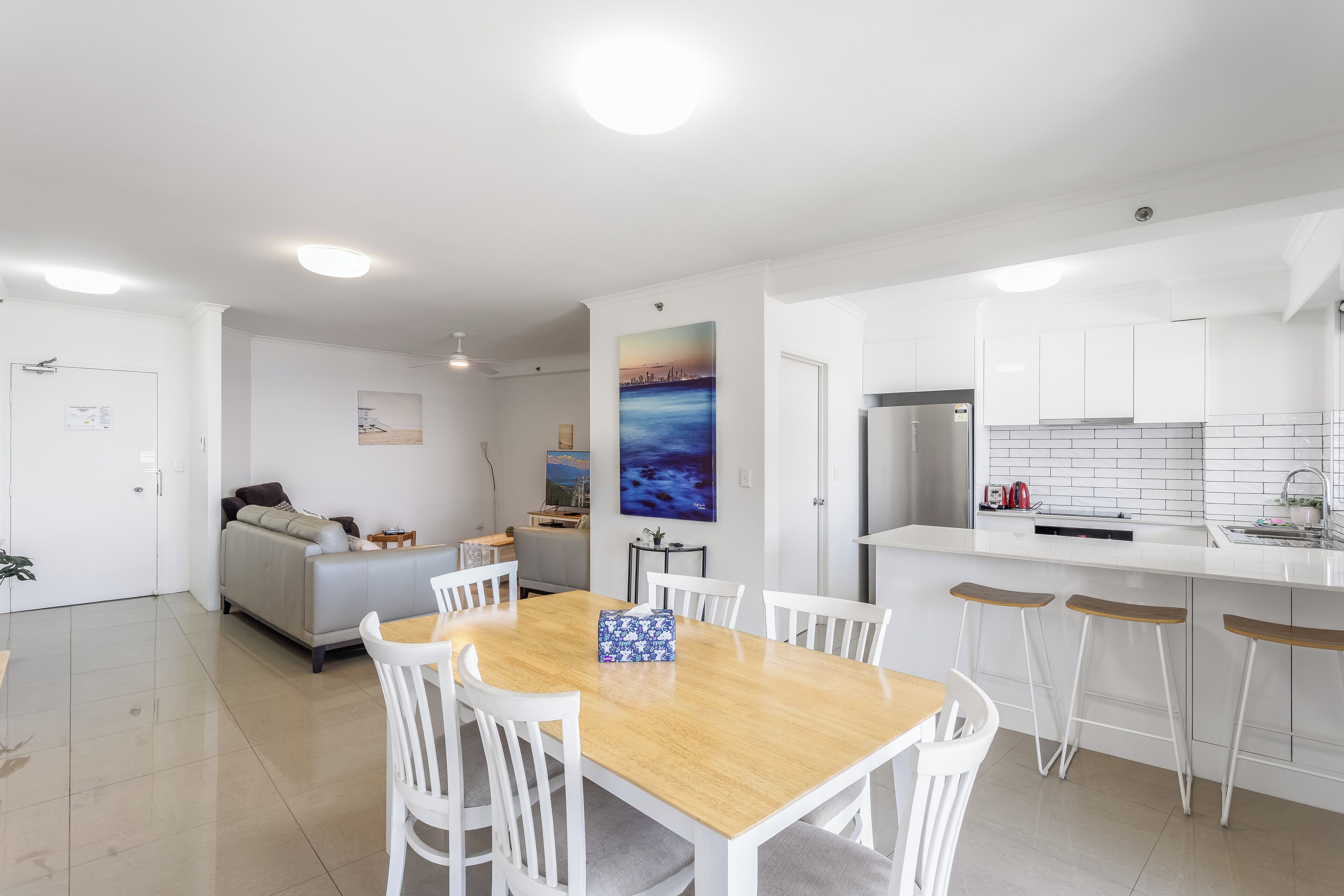 A modern kitchen with white cabinets, a stainless steel refrigerator, and a wooden dining table with white chairs.