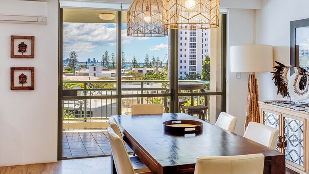 A modern dining area with a large table, chairs, and a view of the city through large windows.