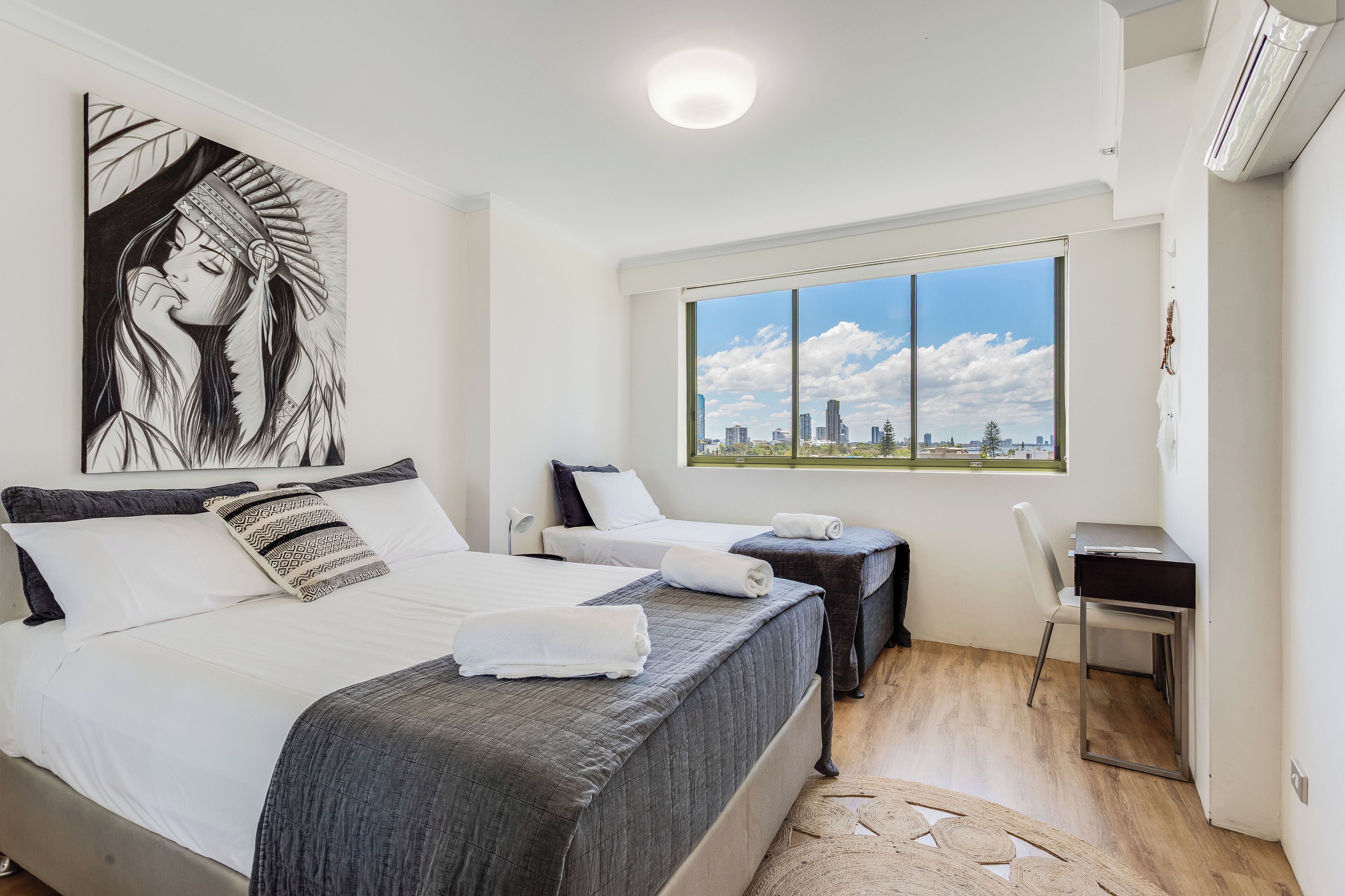 A modern hotel room with a large bed, two bedside tables, a desk, and a large window offering a city view.