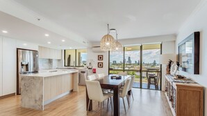 A modern kitchen with a central island, dining area with chairs, and a view of the city through large windows.