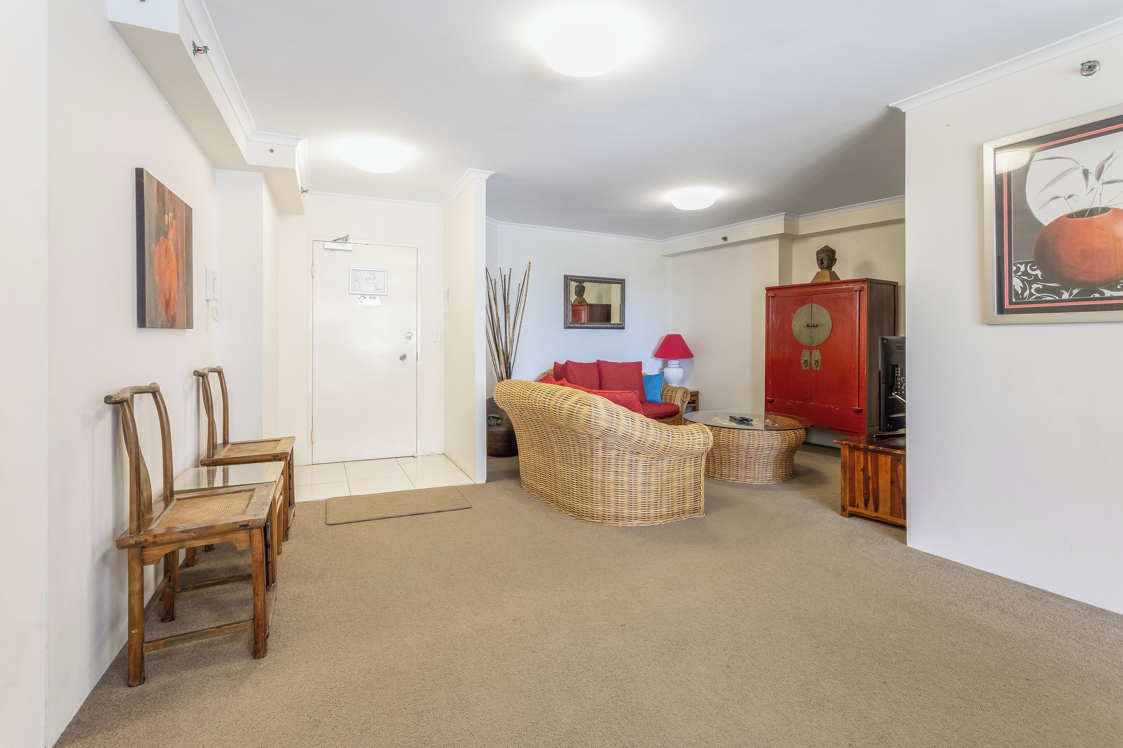 A spacious living room with a sofa, chairs, a red cabinet, and a framed picture on the wall.