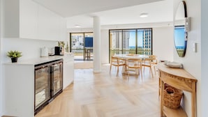 A modern kitchen with white cabinetry, a dining area with a round table and chairs, and large windows offering a view of the city.