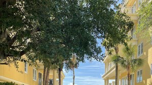 A paved pathway leading to a covered entrance with a pergola, surrounded by well-maintained gardens and palm trees, flanked by yellow buildings with balconies. - 3 bedroom,baths, Pool, Land Trans from Dock, 4 passenger golf cart included! (Daufuskie Island)