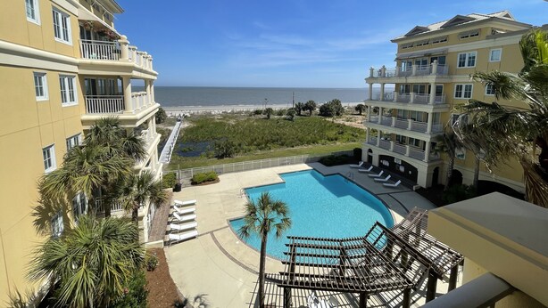 A hotel with a pool, a beach view, and a landscaped area with palm trees. - 3 bedroom,baths, Pool, Land Trans from Dock, 4 passenger golf cart included! (Daufuskie Island)