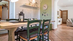 Un coin repas avec une table en bois, des chaises à l’assise verte, une horloge murale et une étagère ornée d’objets décoratifs.
