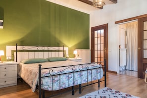 Ein Schlafzimmer mit Bett, Nachttischen, einer grünen Wand, einer Holztür und Blick ins Badezimmer.