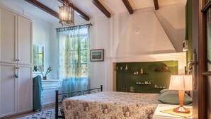 Une chambre à coucher comprenant un lit, une table de chevet, une lampe, une commode, une fenêtre avec des rideaux et un mur vert agrémenté d’étagères.