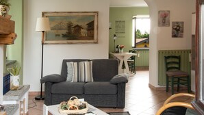 Un salon avec un canapé, une lampe, un tableau et, au fond, un coin repas.