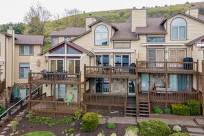 A multi-story residential building with a deck, outdoor seating, and a stone facade. - Cozy Cove Retreat w/ Deck & Fireplace (McHenry)