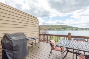 A deck with a table and chairs, a grill cover, and a view of a lake and hills. - Cozy Cove Retreat w/ Deck & Fireplace (McHenry)
