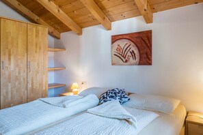 A bedroom with a wooden ceiling, a bed with white bedding, a nightstand with a lamp, and a wooden wardrobe.