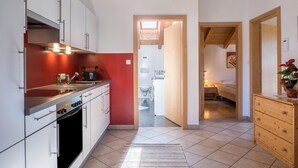 Una cocina compacta con armarios blancos, un horno negro y una pared de acento roja. Se ve un aparador de madera y una pequeña mesa con un florero al frente.