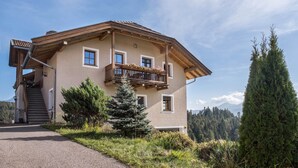 Una casa de dos pisos con un balcón, una escalera y vistas al bosque circundante.