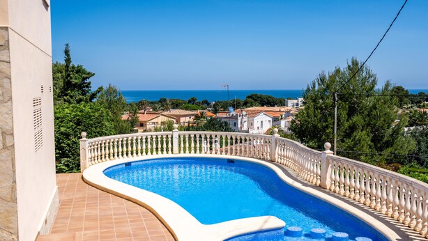 Ein gewundener Swimmingpool mit weißem Geländer, umgeben von einer gefliesten Terrasse und einer Steinmauer.