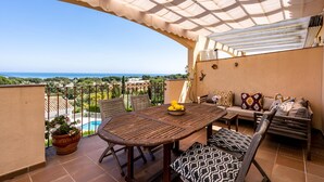 Eine Terrasse mit Tisch, Stühlen und einer Sitzecke mit Blick auf einen Pool und eine schöne Aussicht.
