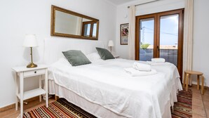 Ein Hotelzimmer mit einem großen Bett, einem Nachttisch, einem Spiegel und Blick durch eine Glastür nach draußen.